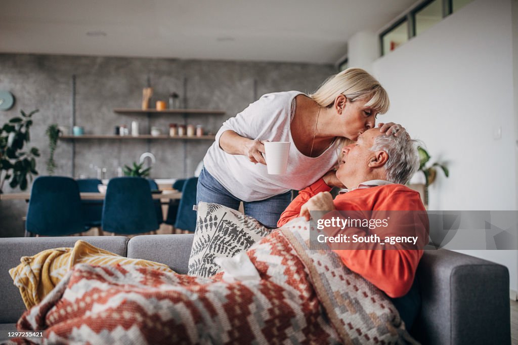Woman kissing her husband on forehead who is ill with flu