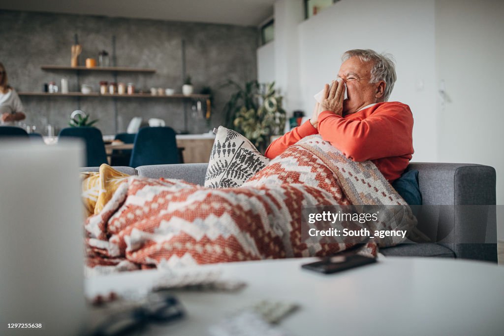 Senior man sick with flu blowing nose