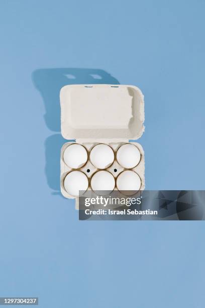 top view of carton containers with white raw chicken eggs on blue background - eierdoos stockfoto's en -beelden