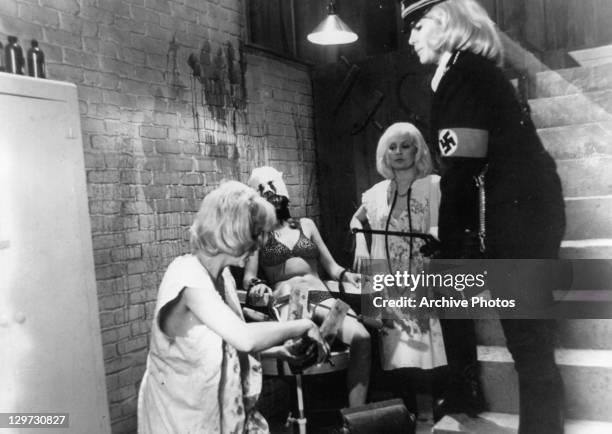 Dyanne Thorne watches women tie another to a chair in a scene from the film 'Ilsa: She Wolf Of The SS', 1975.