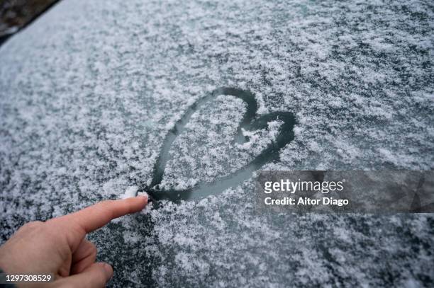 person´s hand painting with his index finger a heart-shaped draw on the snow fallen in a car windshield. - finger painting stock-fotos und bilder