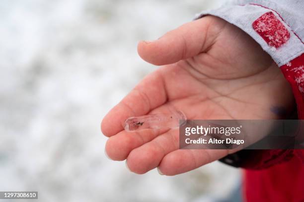 a boy holds a piece of ice in his hand on a winter's day - frostbite fingers stock-fotos und bilder