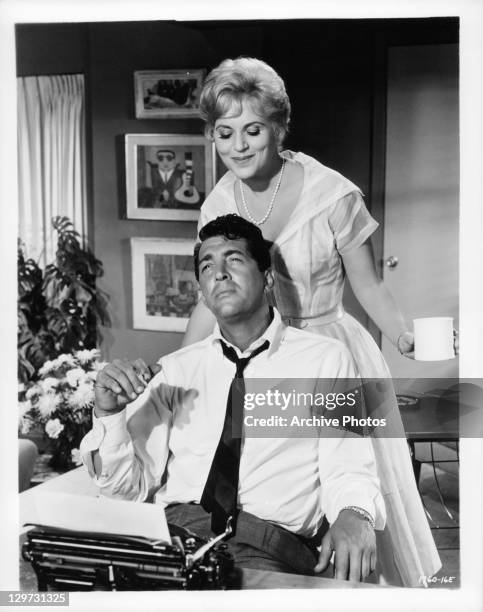 Dean Martin enjoying a cigarette with Judy Holliday behind him in a scene from the film 'Bells Are Ringing', 1960.