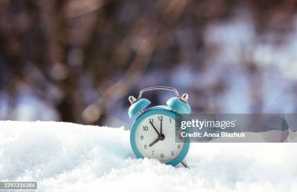 retro alarm clock in snowy sunny day. symbol of winter season, spring forward and daylight saving time. - zona horaria fotografías e imágenes de stock