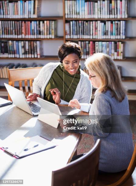 two women with laptops working together in library - public library stock pictures, royalty-free photos & images