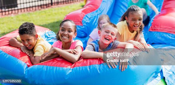 multiethnische kinder auf riesiger aufblasbarer rutsche - inflatable playground stock-fotos und bilder