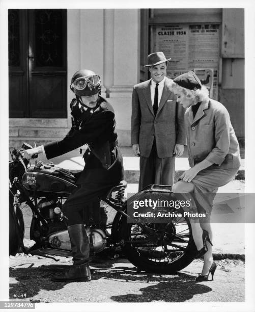 Gene Kelly smiles as Barbara Laage shows leg to French policeman in a scene from the film 'Happy Road', 1957.