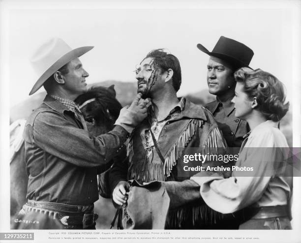 Gene Autry examines Pat Buttram's wound while Kirby Grant and Gail Davis look on in a scene from the film 'Indian Territory', 1950.