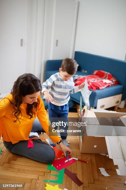 mother with toddler on messy floor making paper craft - child picking up toys stock pictures, royalty-free photos & images