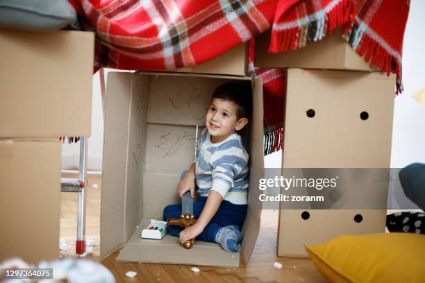 smiling toddler sitting in turned cardboard box with toy sword, imagining he is in fortress - blanket fort stock pictures, royalty-free photos & images
