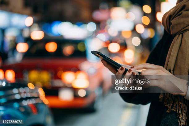 close up of young woman using mobile app device on smartphone to arrange taxi ride in downtown city street, with illuminated busy city traffic scene during rush hour with traffic congestion in the evening - uber　ライドシェア ストックフォトと画像