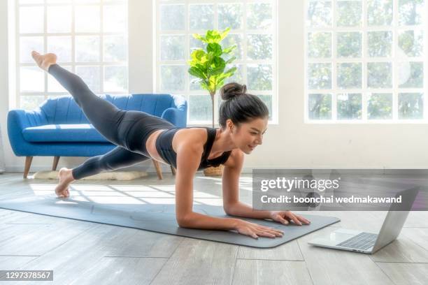 fit woman doing yoga plank and watching online tutorials on laptop, training in living room - home fitness stock pictures, royalty-free photos & images