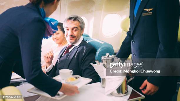 cabin crew serving food to passenger of business class in airplane - airline food stock-fotos und bilder