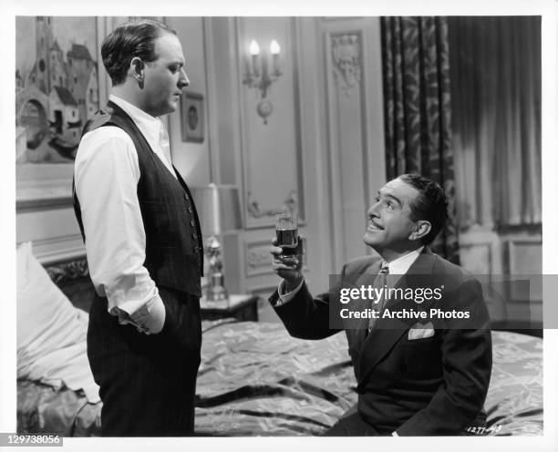 William Gargan looking down at J Carroll Naish, who's sitting on the bed with a drink, in a scene from the film 'Harrigan's Kid', 1943.