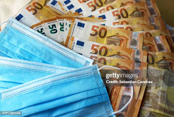 hundred euro bills cash. disposable blue protective masks close up on euro  background. - coronavirus money stock pictures, royalty-free photos & images