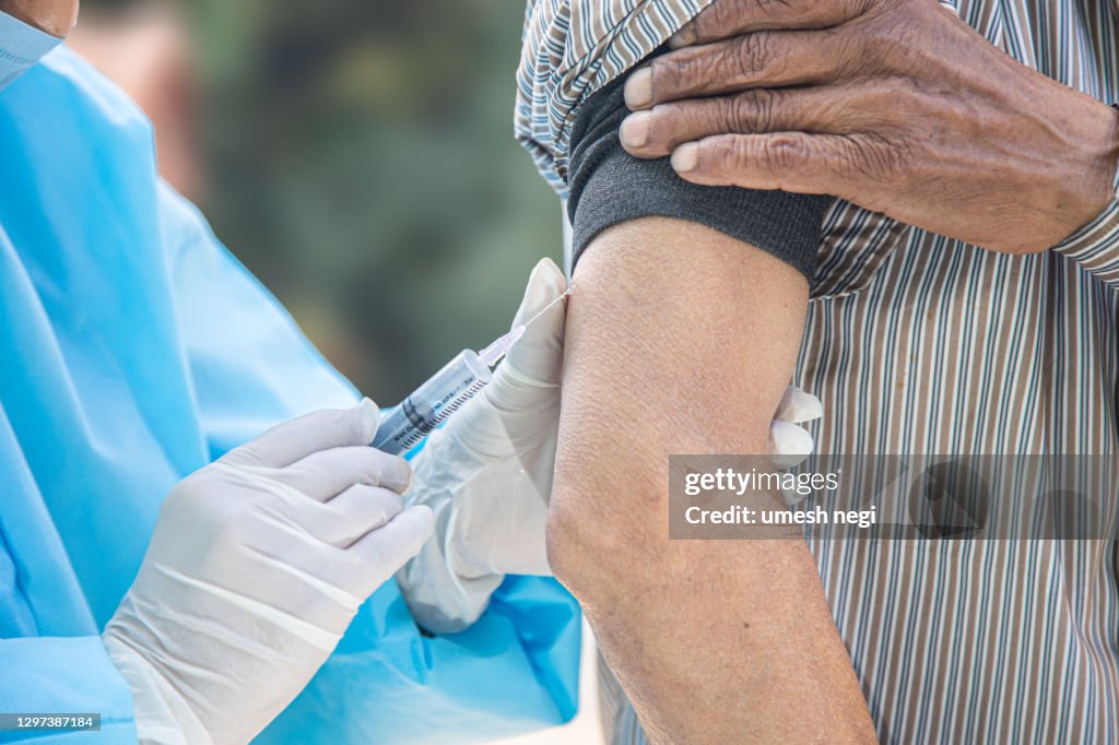 Doctor's hands in surgical gloves preparing COVID-19 vaccine for male patient in India