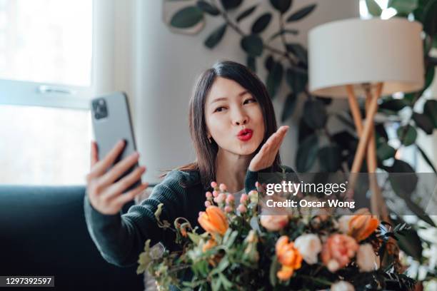 young woman blowing a kiss on video call with her lover - asian couple kissing stockfoto's en -beelden