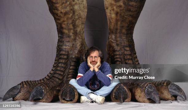 American director Steven Spielberg poses between a pair of giant dinosaur feet in a publicity still for the film 'Jurassic Park', 1993.