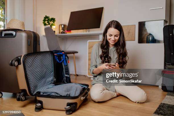 smiling woman using mobile phone - packing suitcase stock pictures, royalty-free photos & images