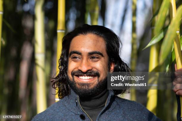 close-up of smiling bearded young man looking away against bamboo trees - asian man long hair stock pictures, royalty-free photos & images