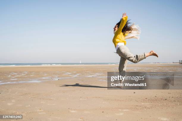 carefree woman jumping at beach against clear sky during sunny day - running netherlands stock pictures, royalty-free photos & images