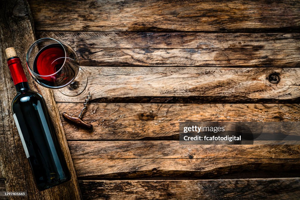 Red wineglass and bottle shot from above on rustic wooden table. Copy space