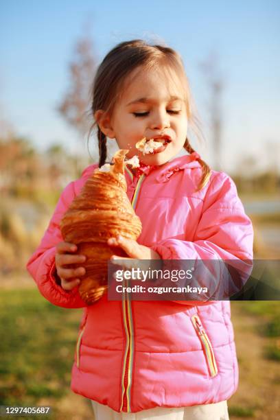 little girl with blond hair eating crispy croissant outdoors on street - eating croissant stock pictures, royalty-free photos & images