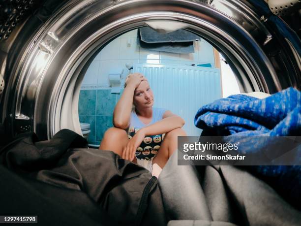 verärgerte frau, die kleidung in waschmaschine im badezimmer anschaut - damaged stock-fotos und bilder