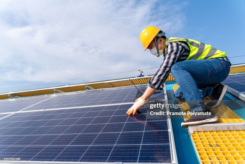 Asian engineer working on checking equipment of solar PV Rooftop on factory roof.