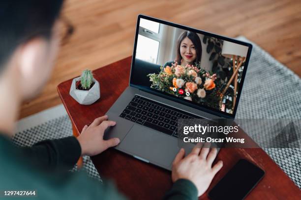 young woman receiving flower bouquet while having a video call with her love - relation à distance photos et images de collection