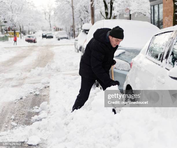 senior man shovelling snow around car on city street. - montreal street stock pictures, royalty-free photos & images
