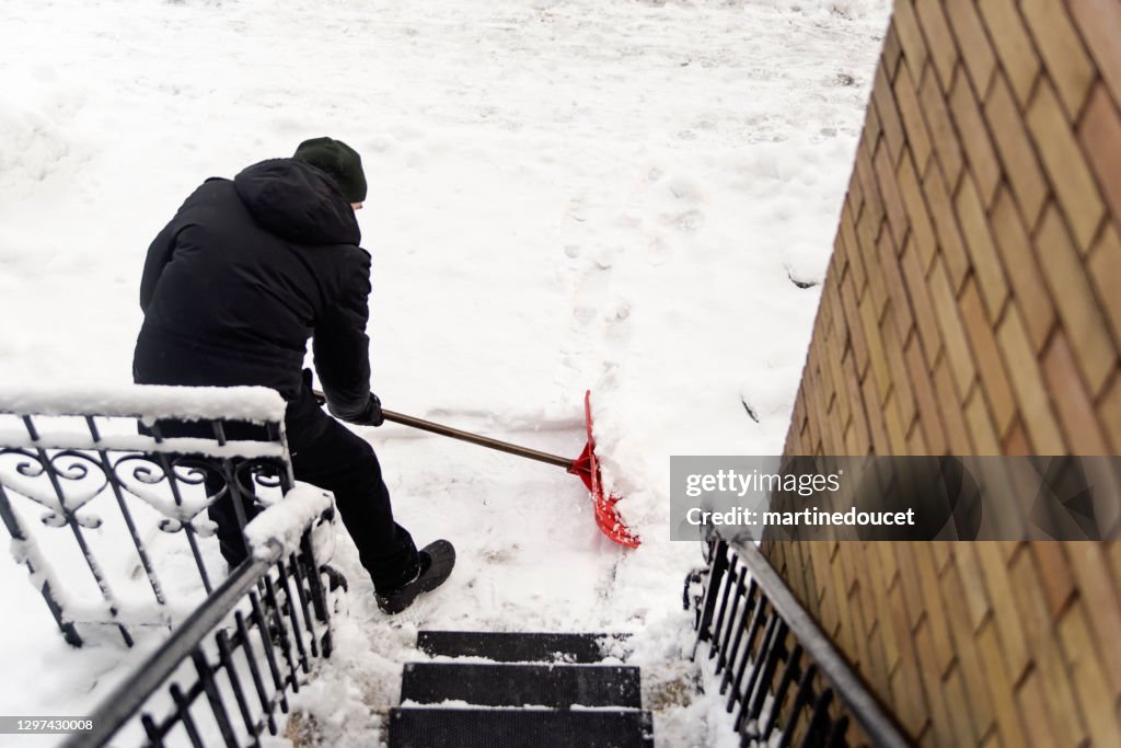 Senior man shoveling snow from stair case on city street.