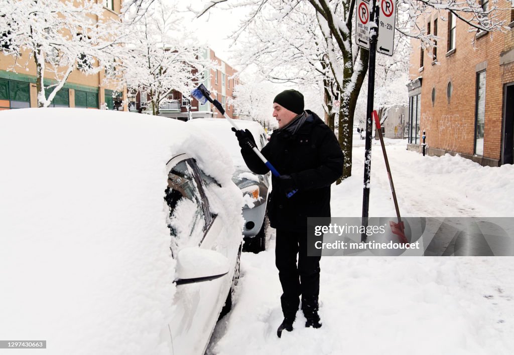 Homme aîné brossant la neige de la voiture sur la rue de ville.
