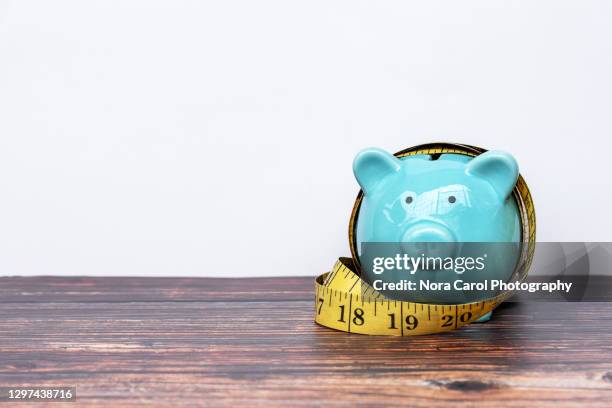 piggy bank and measuring tape - tighten - fotografias e filmes do acervo