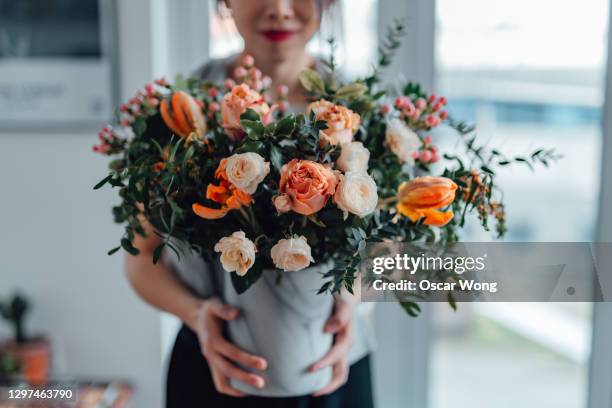 shot of an unrecognisable woman covering her face with flowers in living room - flower bouquet stockfoto's en -beelden