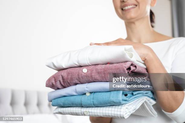 mujer está sosteniendo una pila de camisas planchadas y dobladas - ropa doblada fotografías e imágenes de stock