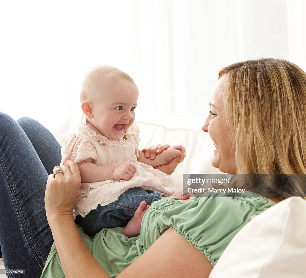 Smiling baby girl and mother on couch.