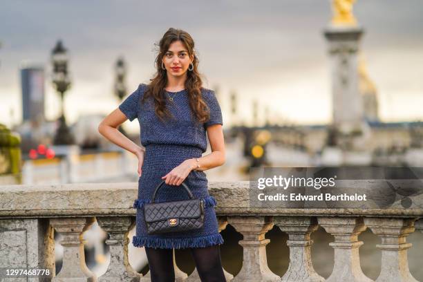 Amanda Derhy wears a necklace, a blue knitted dress with fringes from Maje, black tights, a Chanel bag, on January 17, 2021 in Paris, France.