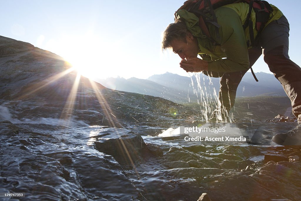 Hiker drinks from mountain stream at sunrise.