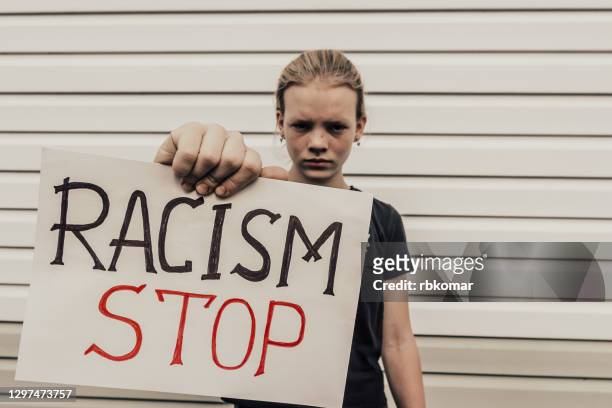 a protest activist holds an anti-racism poster in his hand and looks displeased into the camera. banner - stop racism, ethnic protest, human rights equality concept - anti racism children stock pictures, royalty-free photos & images