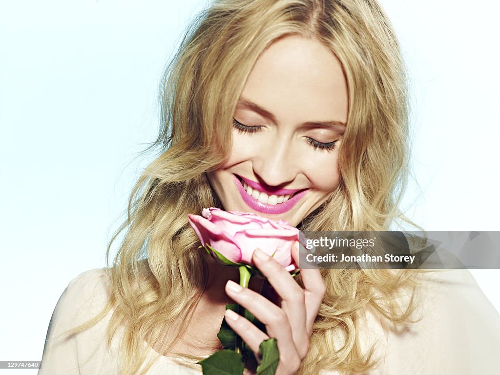 Female holding pink rose to nose with eyes closed.