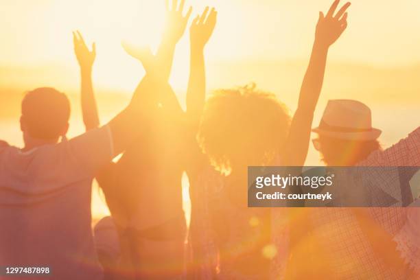 gruppe von freunden sitzen am strand bei sonnenuntergang /sonnenaufgang. - happy dance silhouette stock-fotos und bilder
