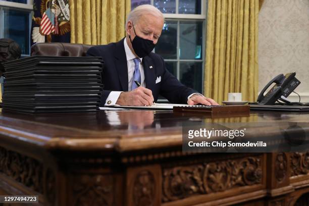 President Joe Biden prepares to sign a series of executive orders at the Resolute Desk in the Oval Office just hours after his inauguration on...