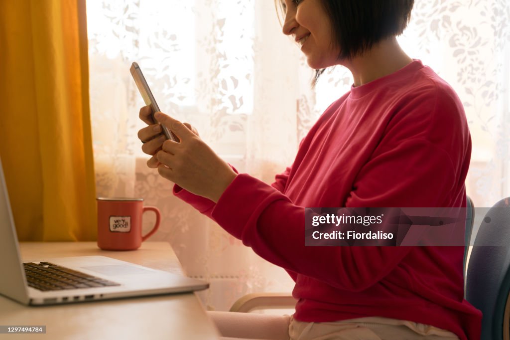 A middle-aged woman in a pink sweater sitting at the table in front of a laptop and a cup of coffee