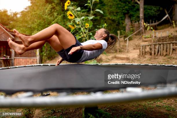 leende ung kvinna på bakgården av hennes hus hoppar på en studsmatta lager foto - trampolin bildbanksfoton och bilder