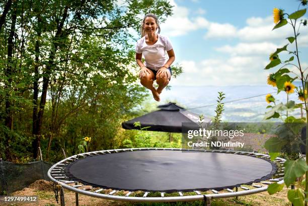 leende ung kvinna på bakgården av hennes hus hoppar på en studsmatta lager foto - trampolin bildbanksfoton och bilder