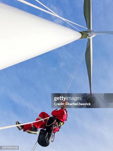 view from bottom wind-turbine and industrial climber rope access technicians abseiling down from blade on the ropes, looking down, dramatic sky and sunny day. - vertigo stock pictures, royalty-free photos & images