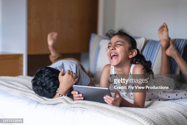 affectionate elementaralter geschwister lachen, während bildschirmzeit auf tablet-computer - australian family time stock-fotos und bilder