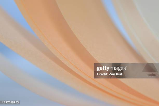 cream colored ribbon unraveling from spool against light blue background - foco difuso fotografías e imágenes de stock