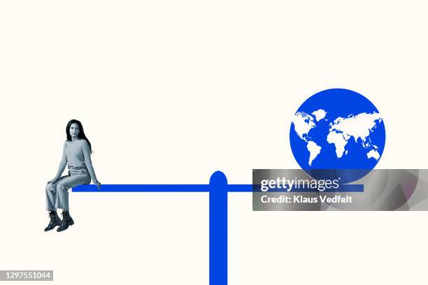 woman sitting with blue planet earth on seesaw - frau globus stock-fotos und bilder